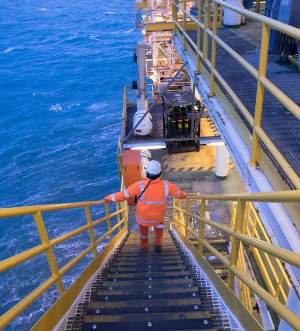 A rig in the distance is reflected in a puddle